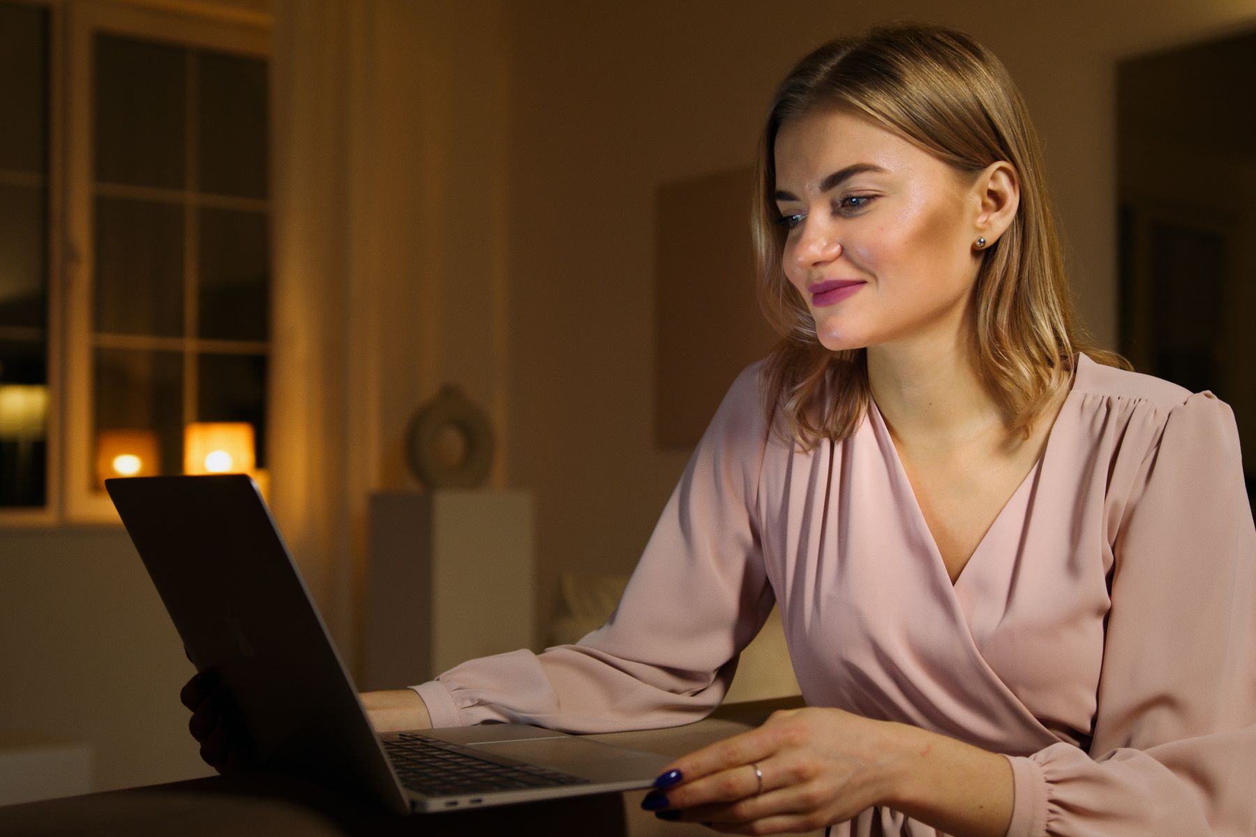 Een vrouw leest glimlachend iets op haar laptop.