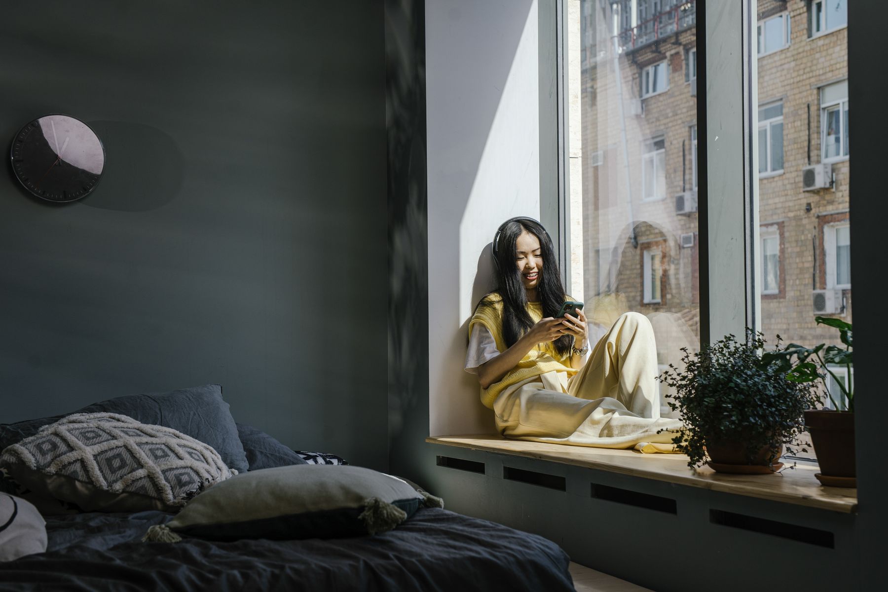 Een vrouw zit bij het raam en kijkt op haar telefoon.